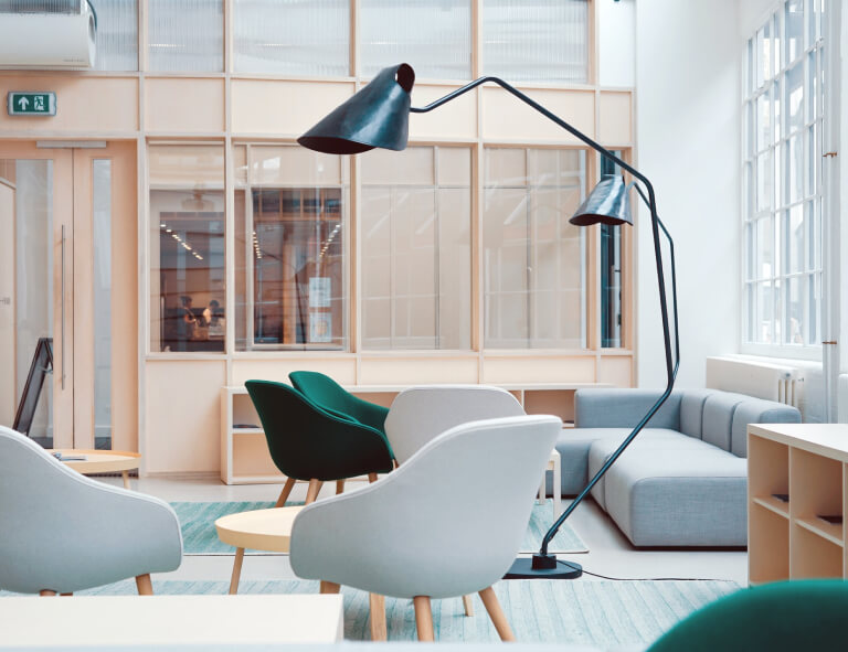 Modern office lounge area with stylish chairs, a sleek floor lamp, and large windows, emphasizing clean and professional design for high-traffic commercial spaces.